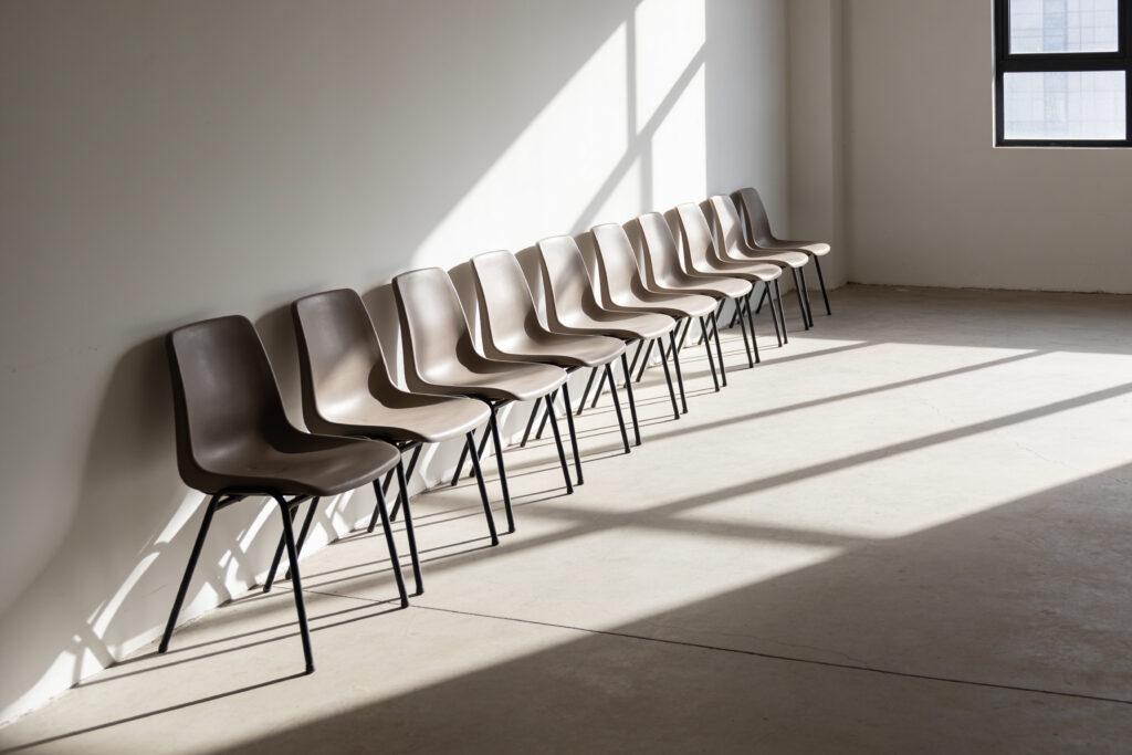 Rangée de chaises identiques face à un mur blanc : l’unanimité de façade en comité de direction